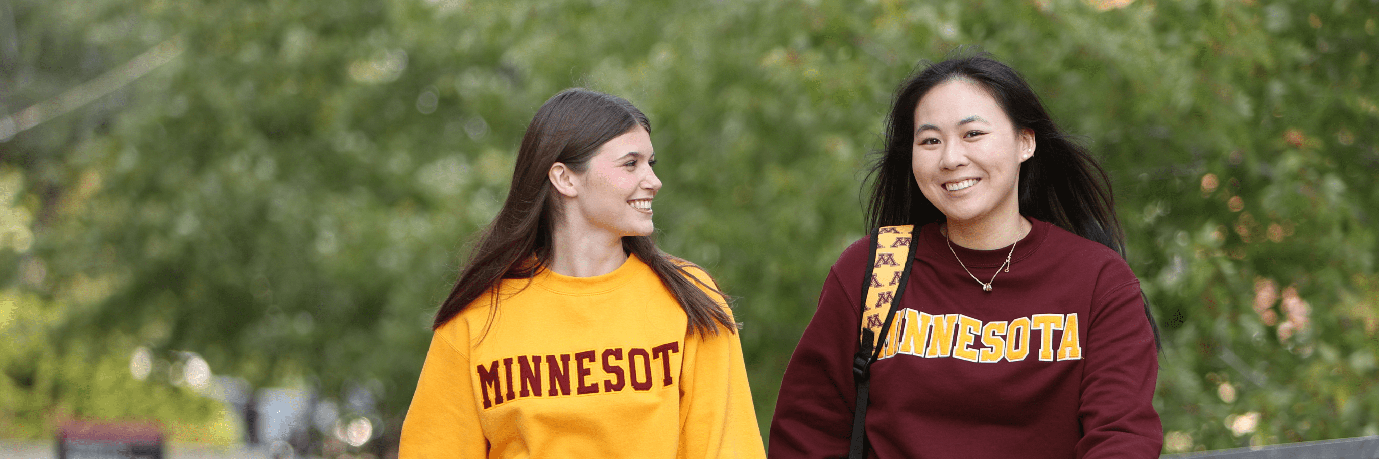 Two students in an outdoor setting wearing UMN merch with positive expressions